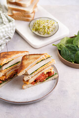 American homemade tall hot grilled cheese sandwich with tofu, cheddar, tomato slices and spinach on white scandi plate cut in triangles. Italian Tramezzini