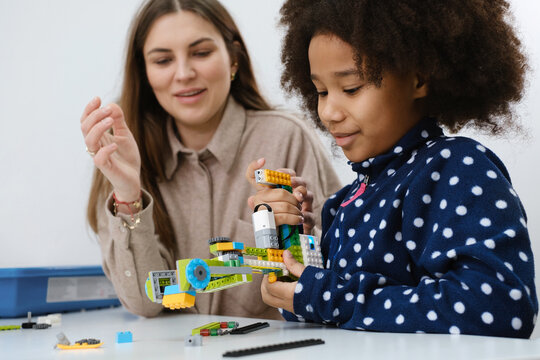 Coding Class, school girl constructing robot arm mechanism. multiethnic children making science, technology tasks with tablet. Modern education African American girl having fun experimenting on lesson