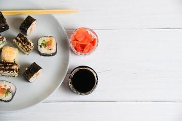 Sushi rolls on a plate on a light gray background, bamboo sticks, soy sauce and ginger, flat lay, copy space