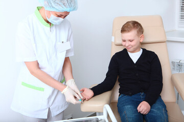 The boy is donating blood in a medical laboratory. A general blood test. Blood from the finger.A...