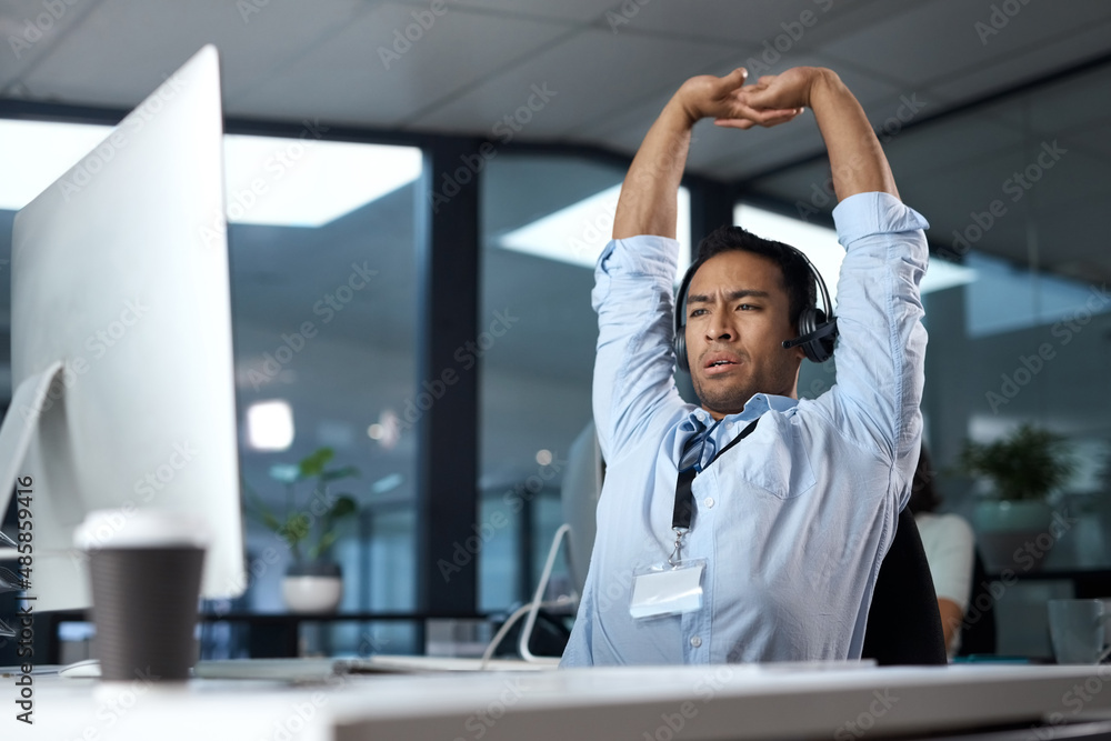 Aufkleber Some calls just make you question your choice in career. Shot of a young man stretching while using a headset and computer in a modern office.