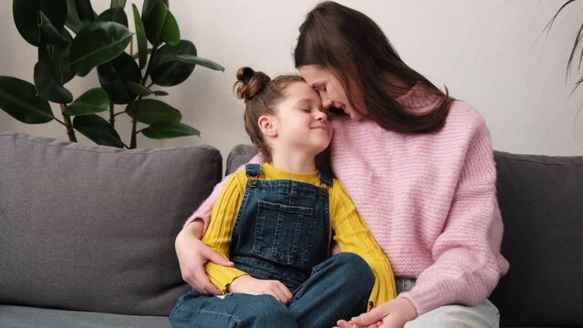 I love you, mom. Loving caring young mother hugging happy cute little child daughter, smiling while sitting together on cozy sofa in living room at home. Family mom and kid enjoying time together