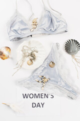 Top view of card with womens day lettering near accessories and blue lingerie on white background