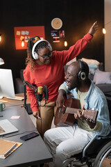 Happy African man with disability playing guitar and singing a song together with woman during live broadcasting