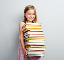 Primary school girl holding stack of books indoors