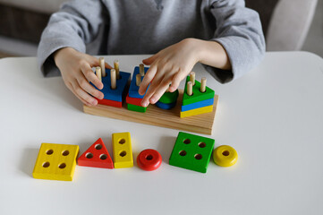 A child plays with a colored educational wooden toy at home.Close-up