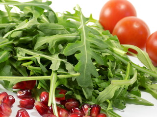 Arugula leaves lie on the table in a pile. In the background are tomatoes.