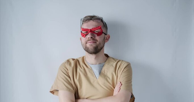 Close up portrait of a male superman doctor or nurse. Portrait of a handsome caucasian male doctor wearing red face superhero mask, eyeglasses and beige medical uniform. High quality 4k video