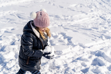 Fototapeta na wymiar Young caucasian preschool girl in warm clothes making big snowball, playing and having fun on sunny winter weather outside on snow covered field in city park. Christmas holidays, childhood, carefree
