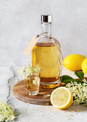 Homemade elderflower liquor in a bottle and glass summer drink with elder flower buds and lemon....