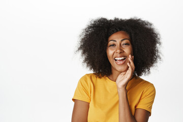 Fototapeta na wymiar Beauty. African american lady laughing and smiling, looking happy, touching clean glowing facial skin, standing over white background
