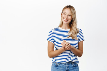 Fototapeta premium People concept. Stylish modern girl, 25 years old, standing in assistant helpful pose, ready to offer help, listening to customer and smiling, standing over white background