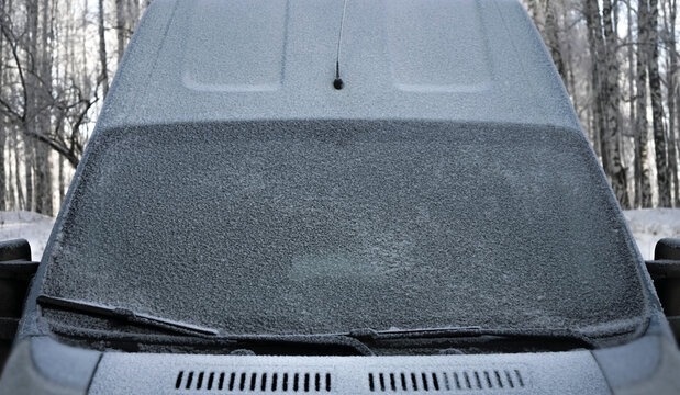 Windscreen wipers and a snow covered car or bus.winter season. front view. A frozen car windshield is covered in ice and snow on a winter day. Close-up view.