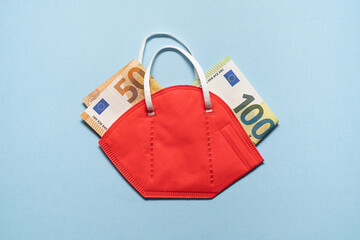 Naklejka premium The Concept of Shopping during the pandemic Covid lockdown. Euro banknotes in red respirator protective masks on blue paper bg.