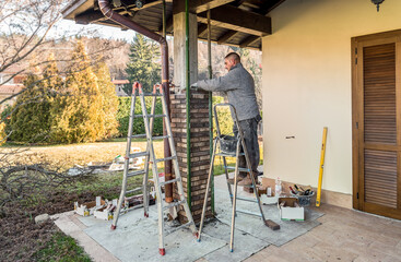 Bricklayer worker installing bricks on the exterior concrete pillar of the house. Construction worker laying bricks.