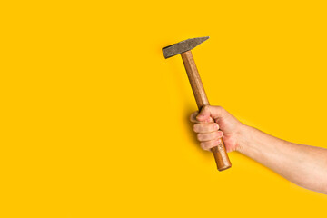 Mano de hombre sosteniendo un martillo sobre un fondo amarillo liso y aislado. Vista de frente y de cerca. Copy space - obrazy, fototapety, plakaty