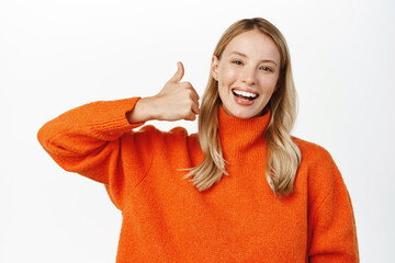 Portrait of smiling blond attractive woman, showing thumbs up in approval, like or recommend,...