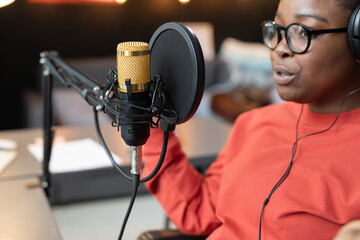 African woman in headphones speaking or singing to the microphone during live broadcasting
