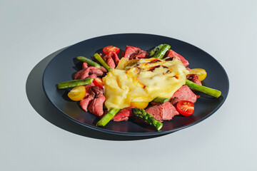 Delicious raclette cheese served over Roast Beef with Tomatoes and Asparagus, dish on white...