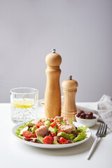 Salad with tuna, lettuce, cucumbers, tomatoes, olives and avocados in white plate on the table