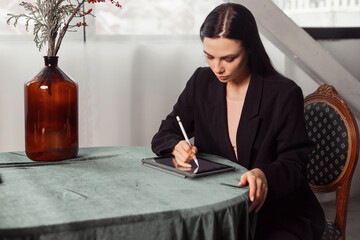 Young brunette freelancer woman designer draws sketches on a graphics tablet using a stylus