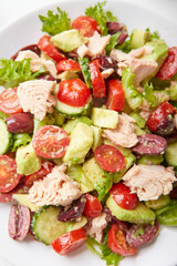 Salad with tuna, lettuce, cucumbers, tomatoes, olives and avocados in white plate on the table
