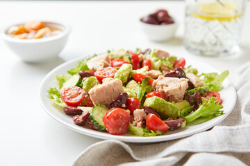 Salad with tuna, lettuce, cucumbers, tomatoes, olives and avocados in white plate on the table