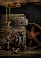 Old pulley, block and tackle, and iron wheel among old barn wood as still life art.