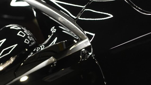 The movement of the camera close up past the door, mirror and hood black shiny car. The process of polishing cars.