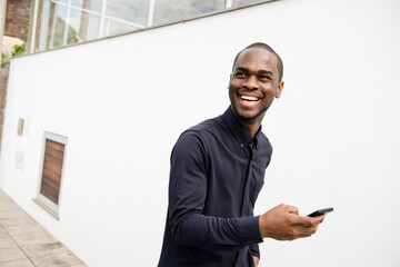 African American man smiling with mobile phone in hand while walking outside