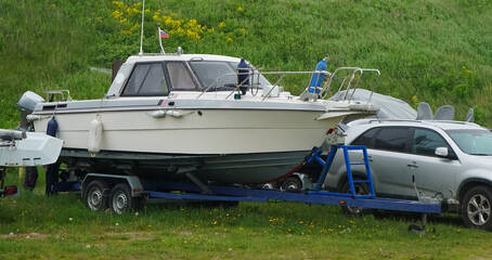 Car transport a big yacht or motor boat near green grass hill.