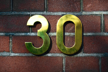 House number 30  (thirty) in golden metal digits on a red brick wall background. - obrazy, fototapety, plakaty