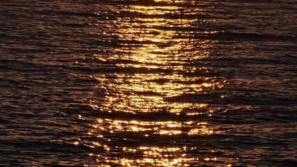 Genova, Italy - January 28, 2022: Beautiful sunset over the sea in winter. Red coloured clouds reflected on the water. Small waves near the the rocks.