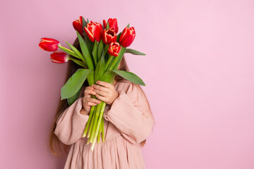 A little cute girl hid behind a bouquet of tulips Pink background. Happy women's day. Space for text. Bright Emotions.