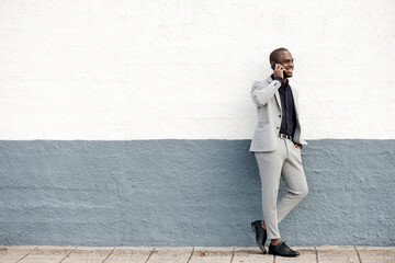 Full body smiling african american businessman standing against wall talking with phone