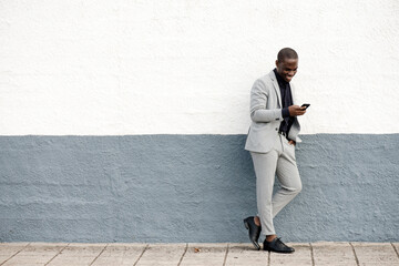 Full body smiling black businessman by wall looking at phone