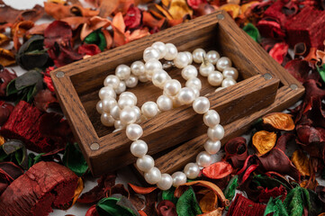 Pearl jewelry in wooden box on dry flowers background.