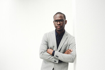 handsome black businessman with glasses leaning against white wall