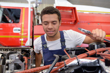 happy male firefighter fixing truck in a fire station