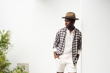 handsome african american man leaning against white wall with shirt and hat