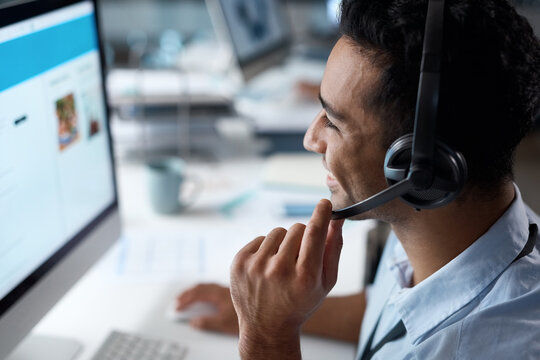 The First Choice In Customer Care. Shot Of A Young Man Using A Headset And Computer In A Modern Office.