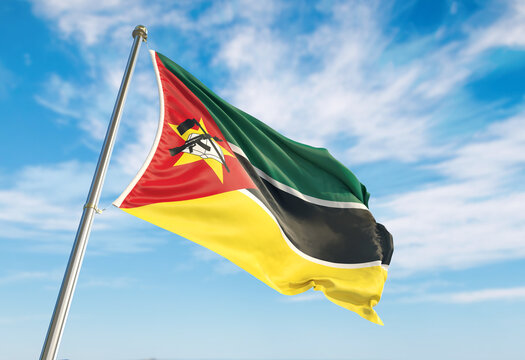 Mozambique flag waving in the wind on flagpole. Mozambique flag waving a blue cloudy sky