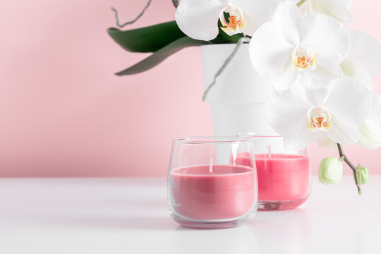 Beautiful flowers composition with white orchid flower and pink candles in glass on pastel pink background. Valentine's day, Happy women's day