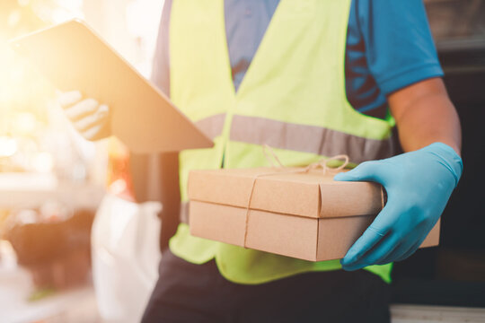 Corona Virus concept Delivery freight forwarder using laptop checks parcel items with protective mask and rubber medical gloves holding parcel boxes for home delivery online
