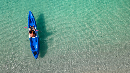 aerial view of man in floating kayak. kayaking out from beach on clear blue sea. right side copy space. water sports and summer recreations. person with life jacket on boat.
