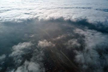 Aerial view from high altitude of distant city covered with puffy cumulus clouds flying by before...