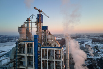 Fototapeta premium Aerial view of cement factory with high concrete plant structure and tower cranes at industrial production area. Greenhouse gas smoke polluting atmosphere. Manufacture and global industry concept.