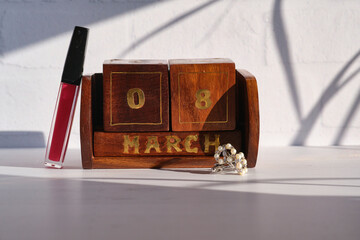 Concept for holiday. International Women's Day. March 8th. Lip gloss, women's cufflinks and Eternal desktop calendar on a light background with space for text or logo.