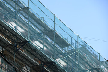 Building facade under renovation works with construction scaffolding frame covered with protective net for workers safety