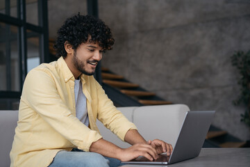 Young Indian freelancer copywriter working from home. Smiling handsome asian programmer using...